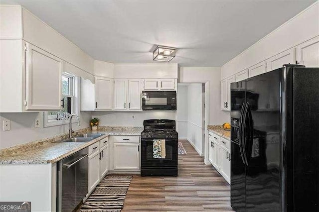 kitchen with black appliances, wood finished floors, a sink, and white cabinets