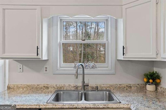 kitchen with light stone countertops, white cabinets, and a sink