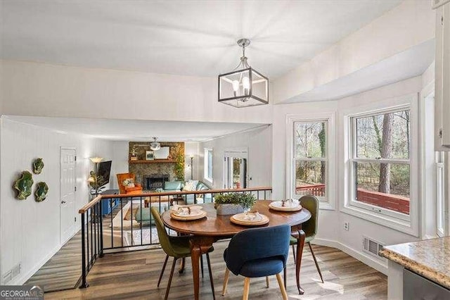 dining area featuring a fireplace, wood finished floors, visible vents, and an inviting chandelier