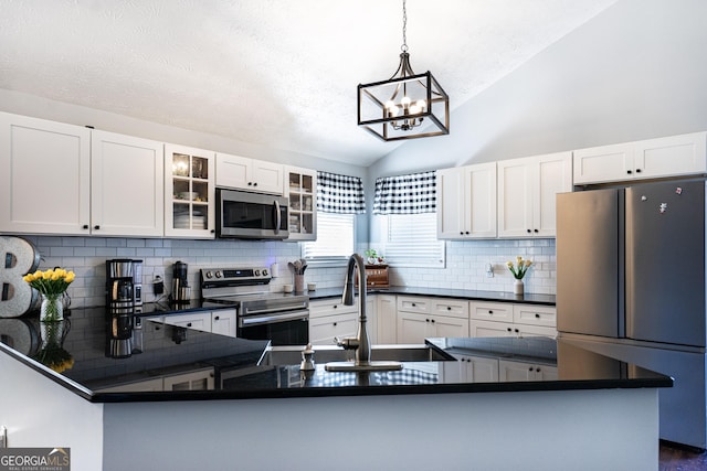 kitchen featuring dark countertops, glass insert cabinets, appliances with stainless steel finishes, vaulted ceiling, and a sink