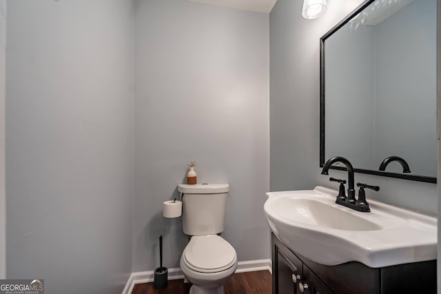 half bath featuring toilet, wood finished floors, vanity, and baseboards