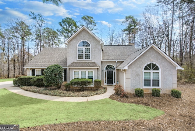 traditional-style home with a chimney, roof with shingles, a front yard, and stucco siding