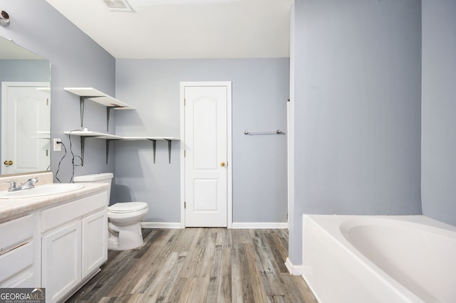 bathroom with toilet, wood finished floors, baseboards, a bath, and vanity