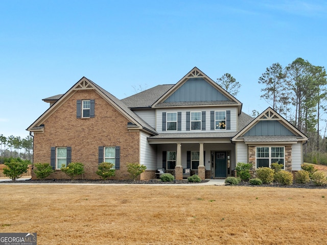 craftsman-style house featuring board and batten siding, covered porch, brick siding, and a front lawn