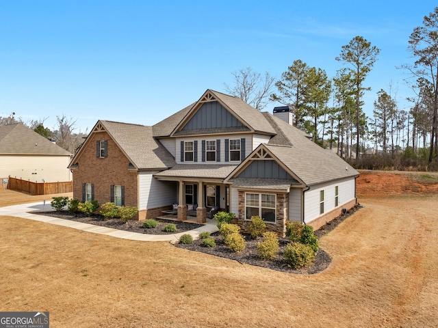 craftsman house with brick siding, fence, roof with shingles, a front lawn, and board and batten siding