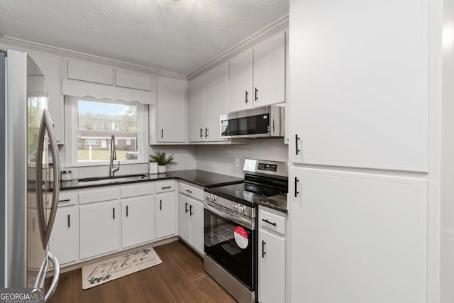 kitchen with stainless steel appliances, a sink, dark wood finished floors, dark countertops, and white cabinetry