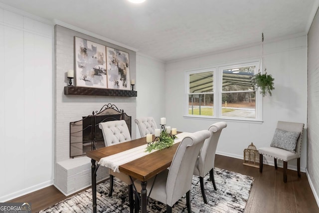 dining room with a brick fireplace, baseboards, dark wood-type flooring, and ornamental molding
