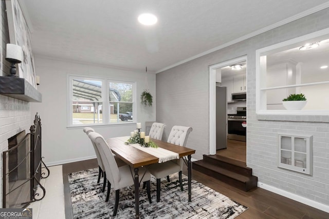 dining area featuring baseboards, a brick fireplace, dark wood-type flooring, and crown molding