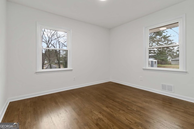 unfurnished room with baseboards, visible vents, and dark wood-style floors