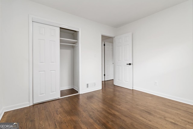 unfurnished bedroom with a closet, wood finished floors, visible vents, and baseboards