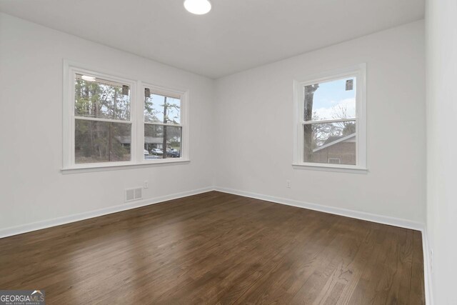 spare room with baseboards, visible vents, and dark wood-style floors