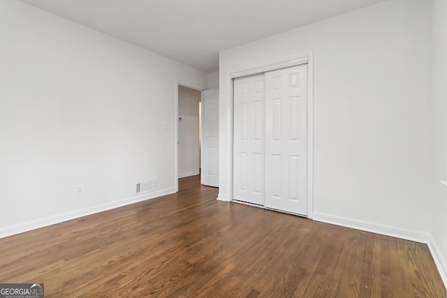 unfurnished bedroom featuring baseboards, wood finished floors, visible vents, and a closet