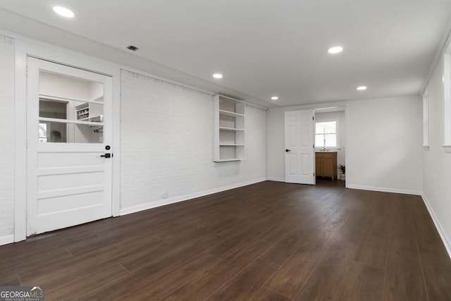 unfurnished living room featuring dark wood-type flooring, baseboards, brick wall, and recessed lighting