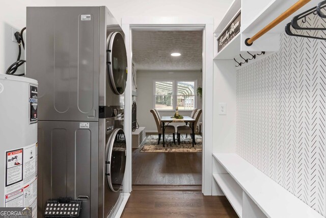 clothes washing area featuring dark wood finished floors, laundry area, stacked washer / dryer, and gas water heater