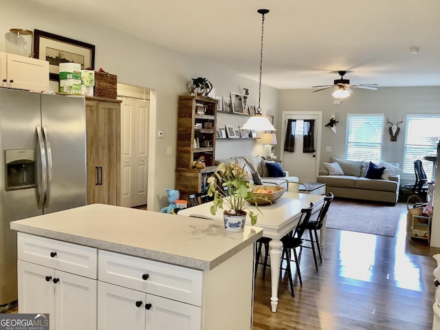 kitchen with wood finished floors, a kitchen island, open floor plan, light countertops, and stainless steel fridge