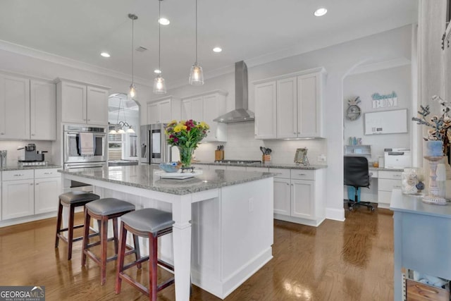 kitchen with wall chimney range hood, dark wood-style floors, a kitchen island, white cabinets, and appliances with stainless steel finishes