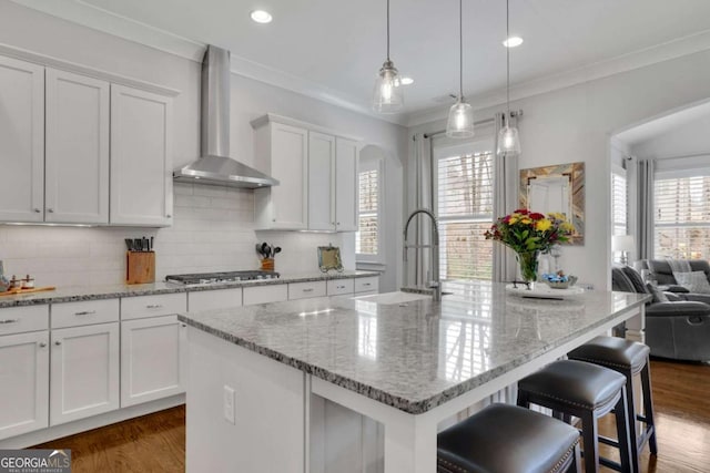 kitchen with white cabinets, a sink, wall chimney range hood, dark wood-style floors, and decorative backsplash