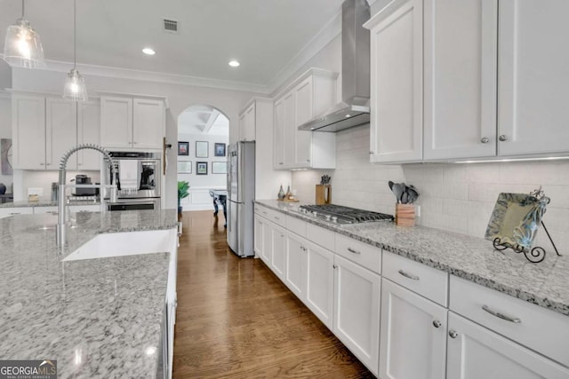 kitchen with visible vents, arched walkways, wall chimney range hood, appliances with stainless steel finishes, and white cabinetry