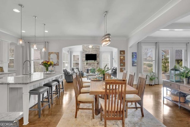 dining space with crown molding, arched walkways, light wood-type flooring, a stone fireplace, and recessed lighting