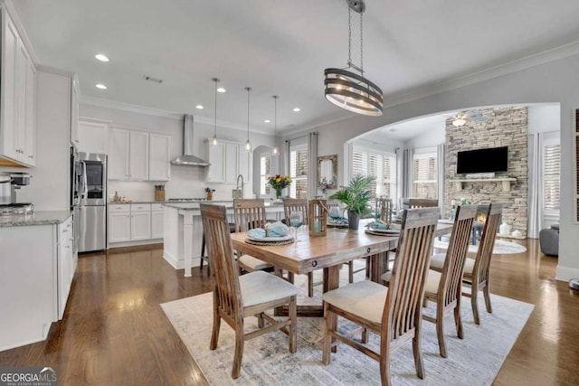 dining area featuring dark wood-type flooring, arched walkways, crown molding, and recessed lighting