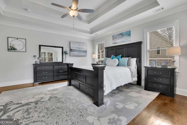 bedroom with ornamental molding, visible vents, wood finished floors, a raised ceiling, and baseboards