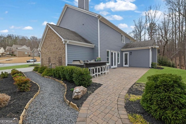 rear view of property featuring a patio, brick siding, outdoor dry bar, and a chimney