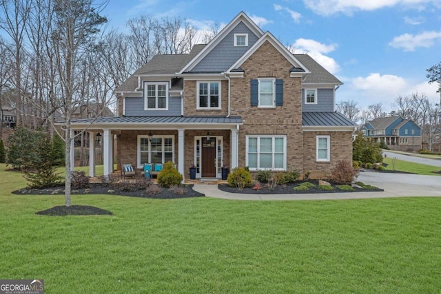 view of front of home with a front yard, brick siding, a standing seam roof, metal roof, and covered porch