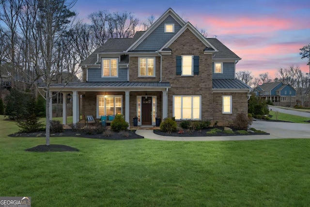view of front of home featuring a yard, covered porch, metal roof, brick siding, and a standing seam roof
