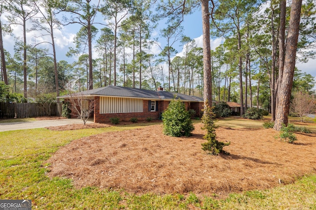 view of front of property with brick siding, a chimney, fence, driveway, and a front lawn