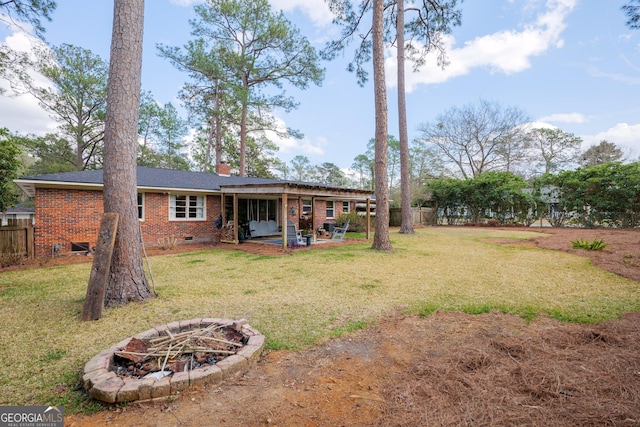 back of house featuring crawl space, brick siding, fence, and a lawn