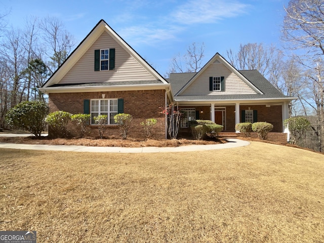 traditional-style home with a porch, brick siding, a shingled roof, and a front lawn