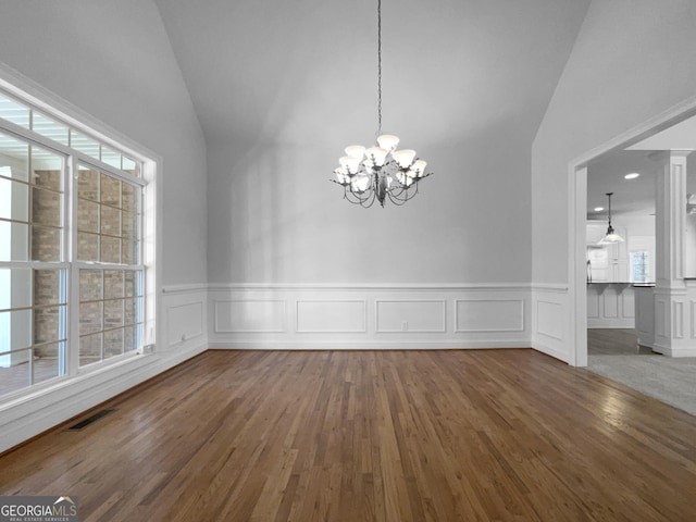 unfurnished dining area with lofted ceiling, visible vents, a notable chandelier, and wood finished floors