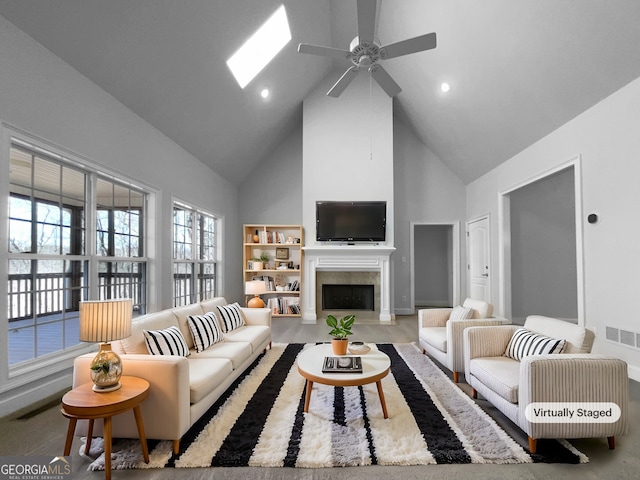 living room featuring a skylight, ceiling fan, a fireplace, and high vaulted ceiling