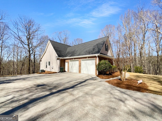 view of home's exterior featuring brick siding, roof with shingles, concrete driveway, a garage, and cooling unit