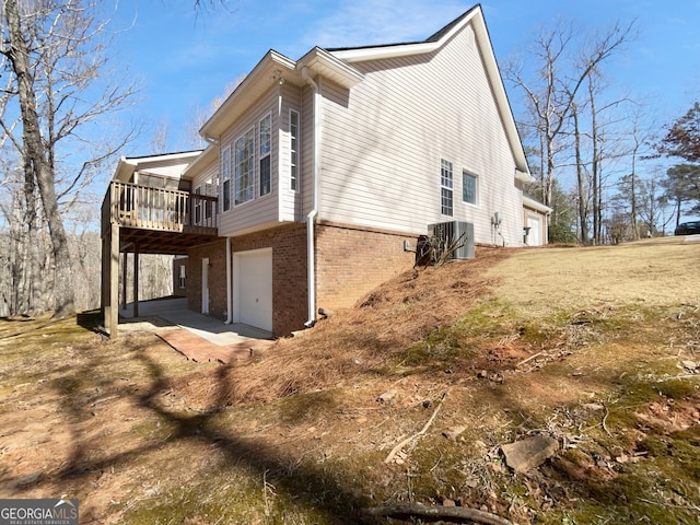 view of side of home featuring a garage, a wooden deck, central AC, and brick siding