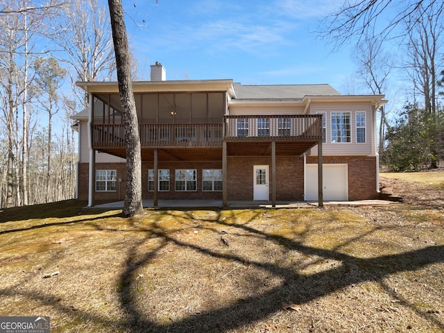 rear view of property with brick siding, a patio, a chimney, an attached garage, and a wooden deck