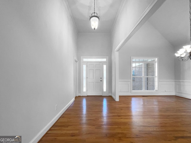 entrance foyer featuring wood finished floors, a wainscoted wall, a decorative wall, and an inviting chandelier