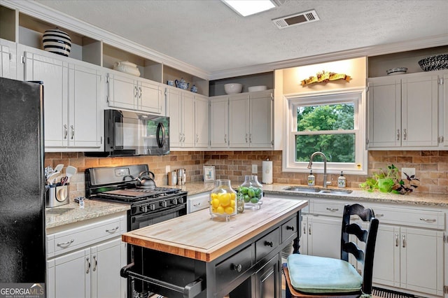 kitchen with butcher block countertops, a sink, visible vents, backsplash, and black appliances