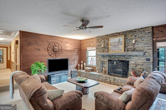 carpeted living area with visible vents, a ceiling fan, wood walls, a stone fireplace, and a textured ceiling