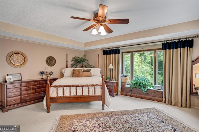 carpeted bedroom with a textured ceiling, ceiling fan, ornamental molding, and a raised ceiling