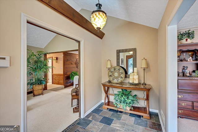 carpeted foyer featuring lofted ceiling, stone finish flooring, baseboards, and a textured ceiling