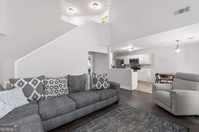 living room with a towering ceiling, wood finished floors, visible vents, and baseboards