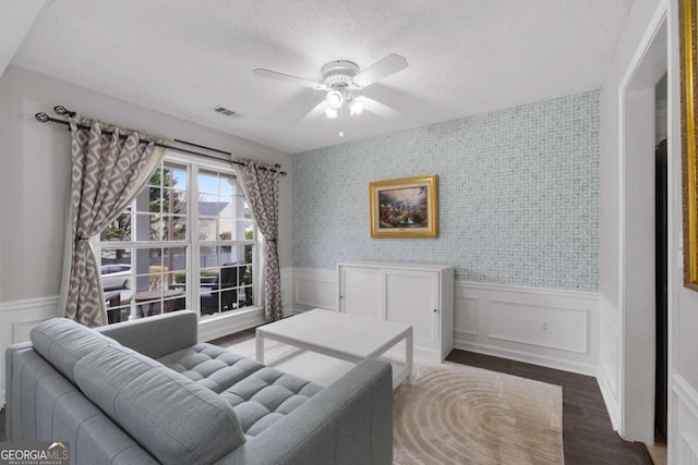 living room with dark wood-style floors, visible vents, a textured ceiling, and wainscoting