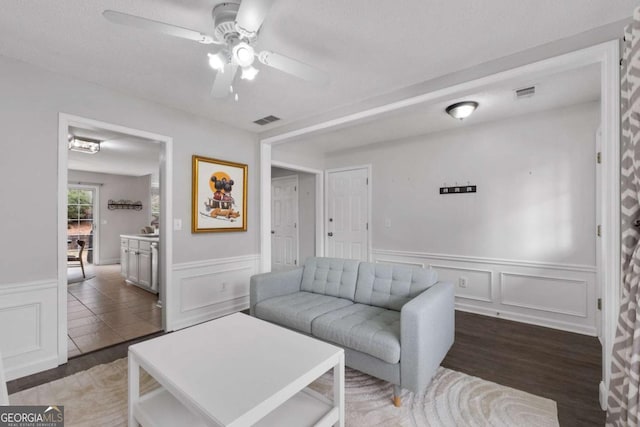 living room with ceiling fan, wainscoting, wood finished floors, and visible vents