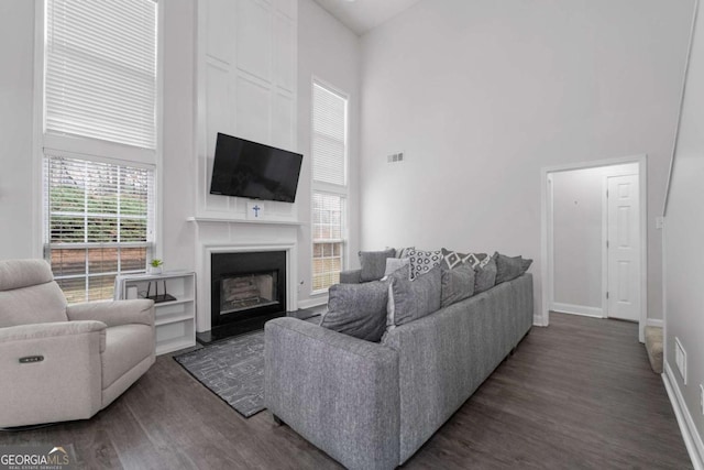 living area with a large fireplace, baseboards, visible vents, a towering ceiling, and dark wood-style floors