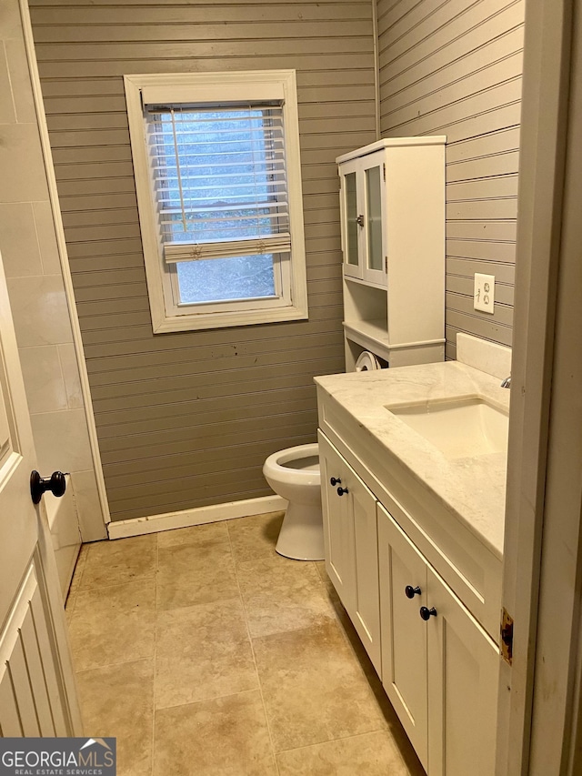 bathroom featuring toilet, wood walls, and vanity
