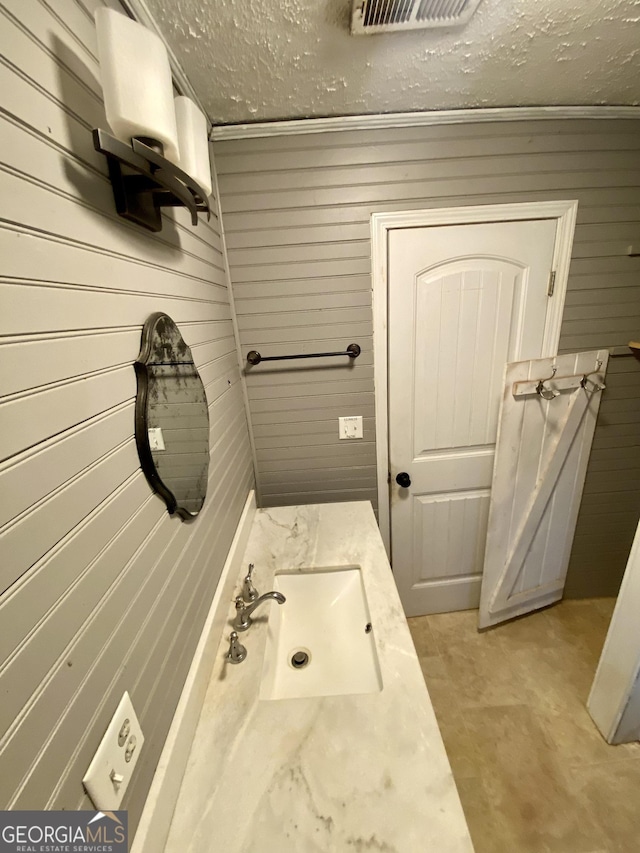 bathroom featuring visible vents, wood walls, concrete flooring, a textured ceiling, and a sink