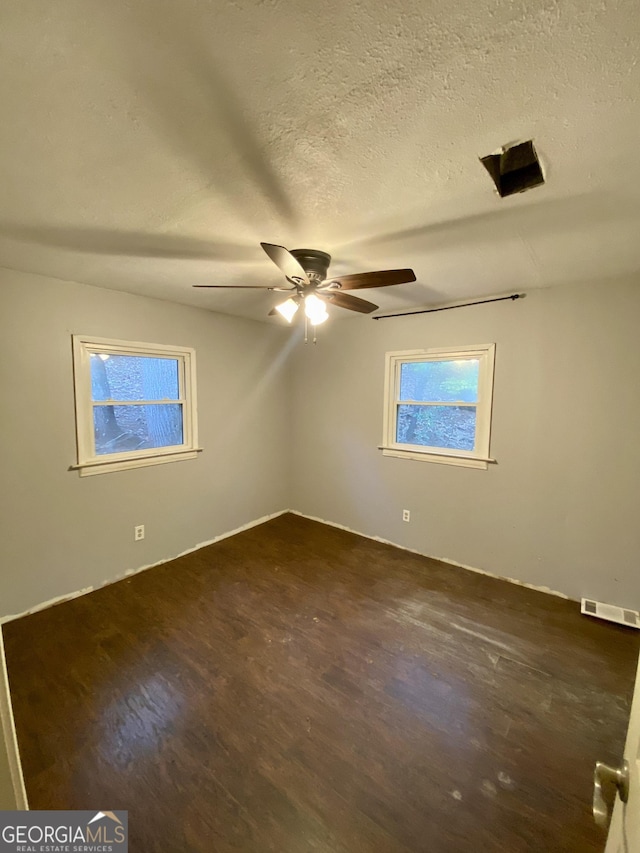 spare room with a ceiling fan, a textured ceiling, visible vents, and dark wood-type flooring