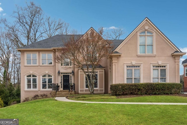 view of front of property featuring a shingled roof, a front yard, and stucco siding