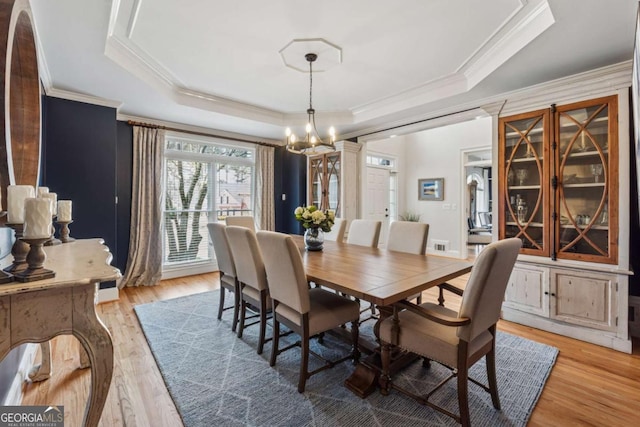 dining area with light wood-style floors, a tray ceiling, ornamental molding, and an inviting chandelier